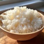 Close-up of fluffy, perfectly cooked sushi rice mounded high in a light wooden bowl.