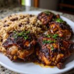Close-up of juicy Jamaican jerk chicken thighs served with rice and peas, garnished with fresh herbs.