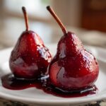 Close-up of two glistening, deep red wine poached pears served on a white plate with syrup.