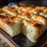 Close-up of fluffy, golden-brown sheet pan pancakes cut into individual squares on a dark baking tray.