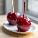 Two glossy, deep red candy apples sitting on a white plate, showcasing the crack-free coating.