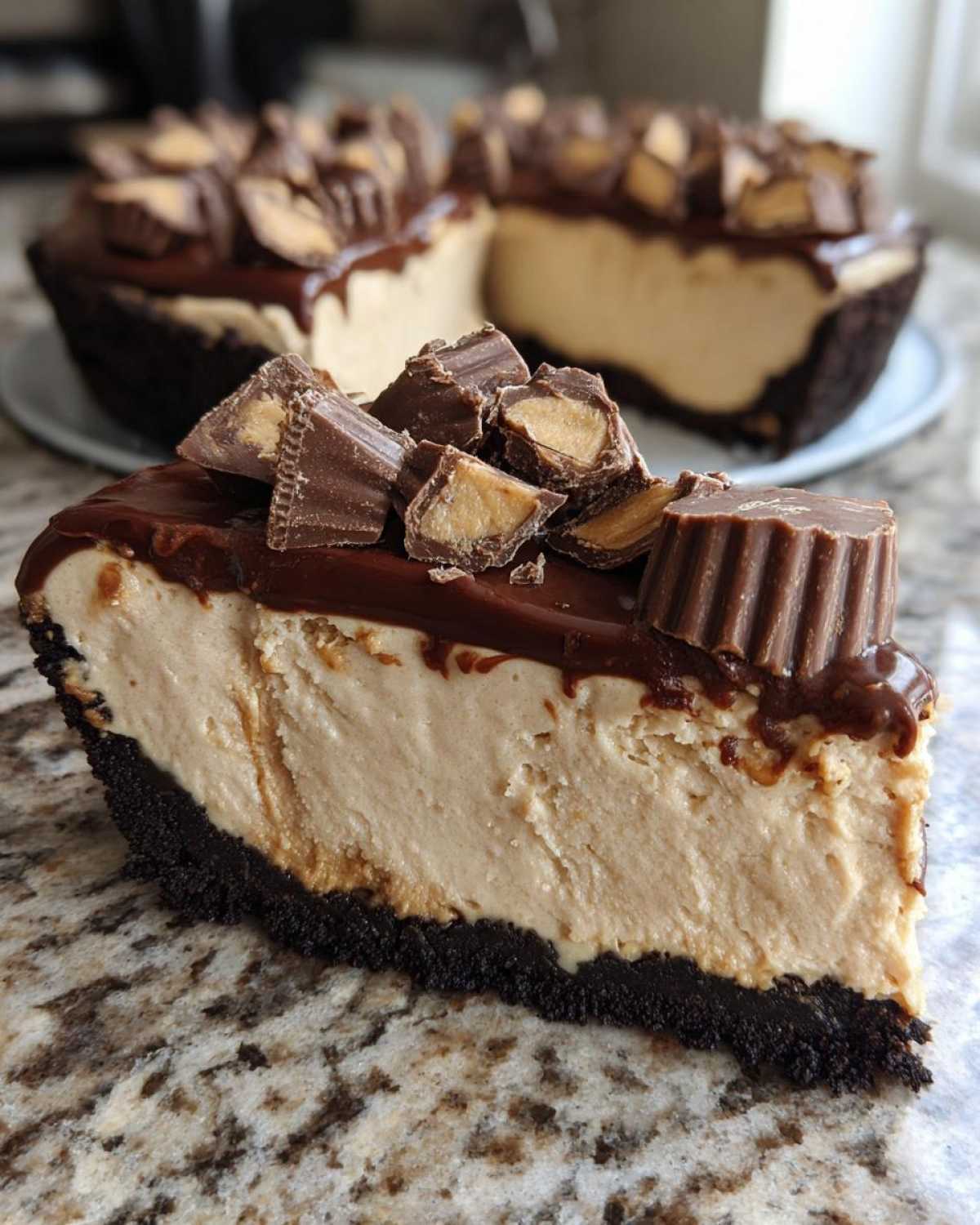 A thick slice of no-bake peanut butter pie with a dark chocolate crust, topped with fudge and chopped peanut butter cups.