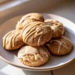 A stack of soft cinnamon applesauce cookies drizzled with a light brown glaze, sitting on a pale plate.