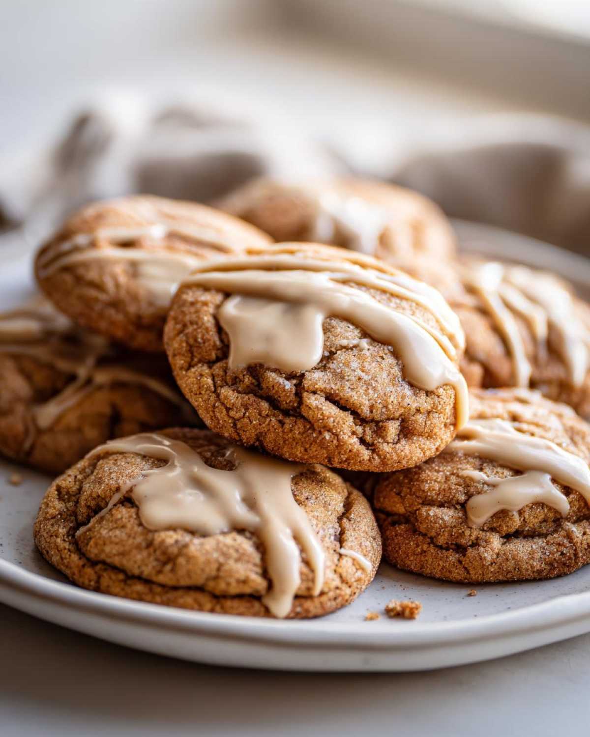 A stack of soft cinnamon applesauce cookies drizzled with a light brown glaze on a white plate.