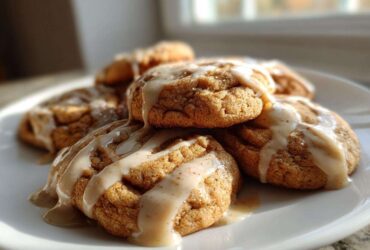 A stack of soft cinnamon applesauce cookies drizzled generously with a light brown glaze, sitting on a white plate.
