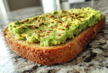 Close-up of creamy avocado toast topped with red pepper flakes, sitting on a granite countertop.