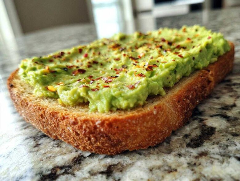 Close-up of creamy avocado toast topped with red pepper flakes, sitting on a granite countertop.