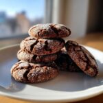 A stack of dark, crinkly gingersnap cookies coated in granulated sugar, sitting on a white plate.
