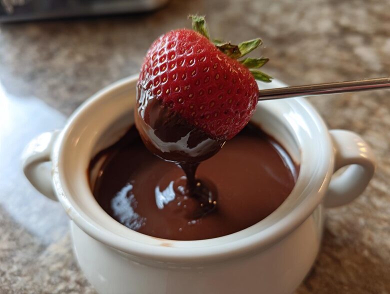 A fresh strawberry being dipped into a small white pot of smooth, melted chocolate fondue.