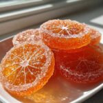 Close-up of glistening, bright orange candied orange slices heavily coated in white sugar crystals.