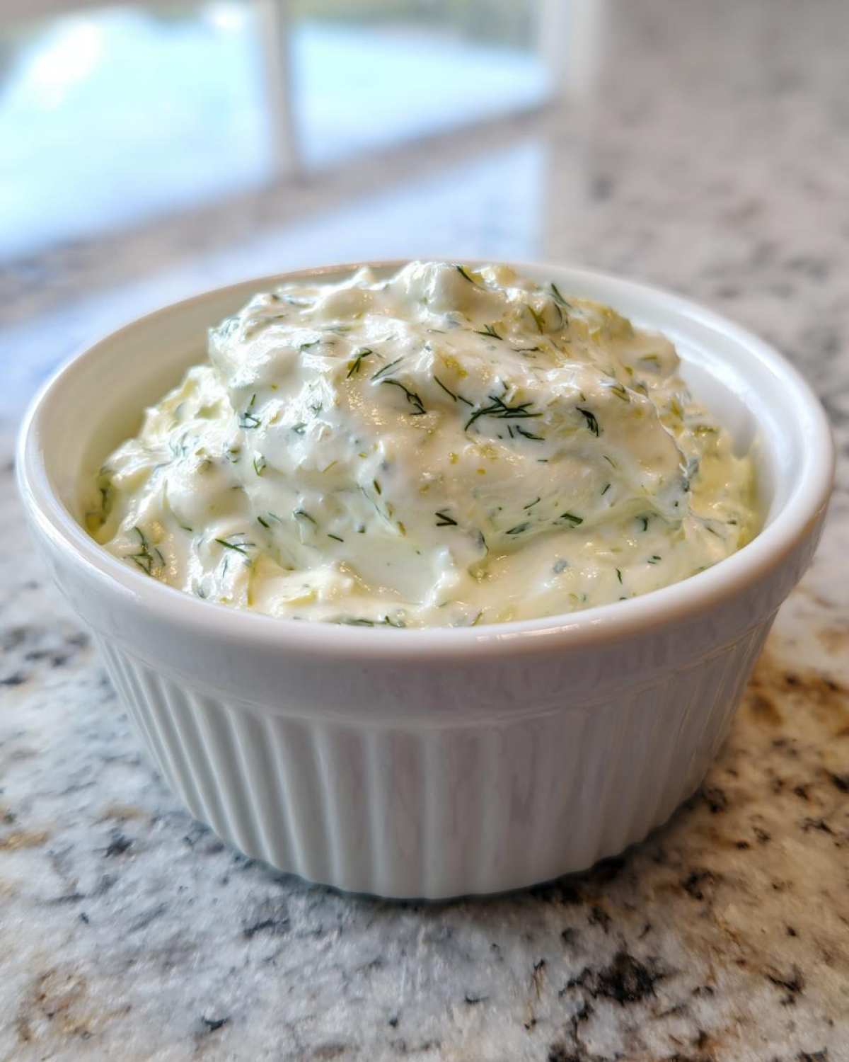 Close-up of creamy, homemade tartar sauce recipe with visible dill and relish in a white fluted ramekin.
