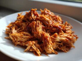 Close-up of tender, saucy pulled chicken piled high on a white plate, ready to serve.