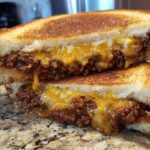 Close-up of a cheesy texas toast sloppy joes sandwich cut in half, showing melted cheddar and ground beef filling.