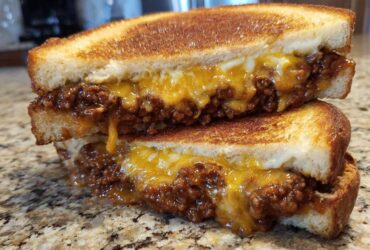 Close-up of a cheesy texas toast sloppy joes sandwich cut in half, showing melted cheddar and ground beef filling.