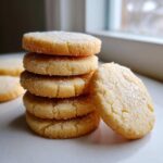 A close-up stack of five thick, round sugar cookies topped with coarse sugar crystals, leaning against one cookie.