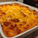 A close-up of a hot, bubbly 3 ingredient chili cheese dip topped with melted, browned cheddar cheese in a white baking dish.