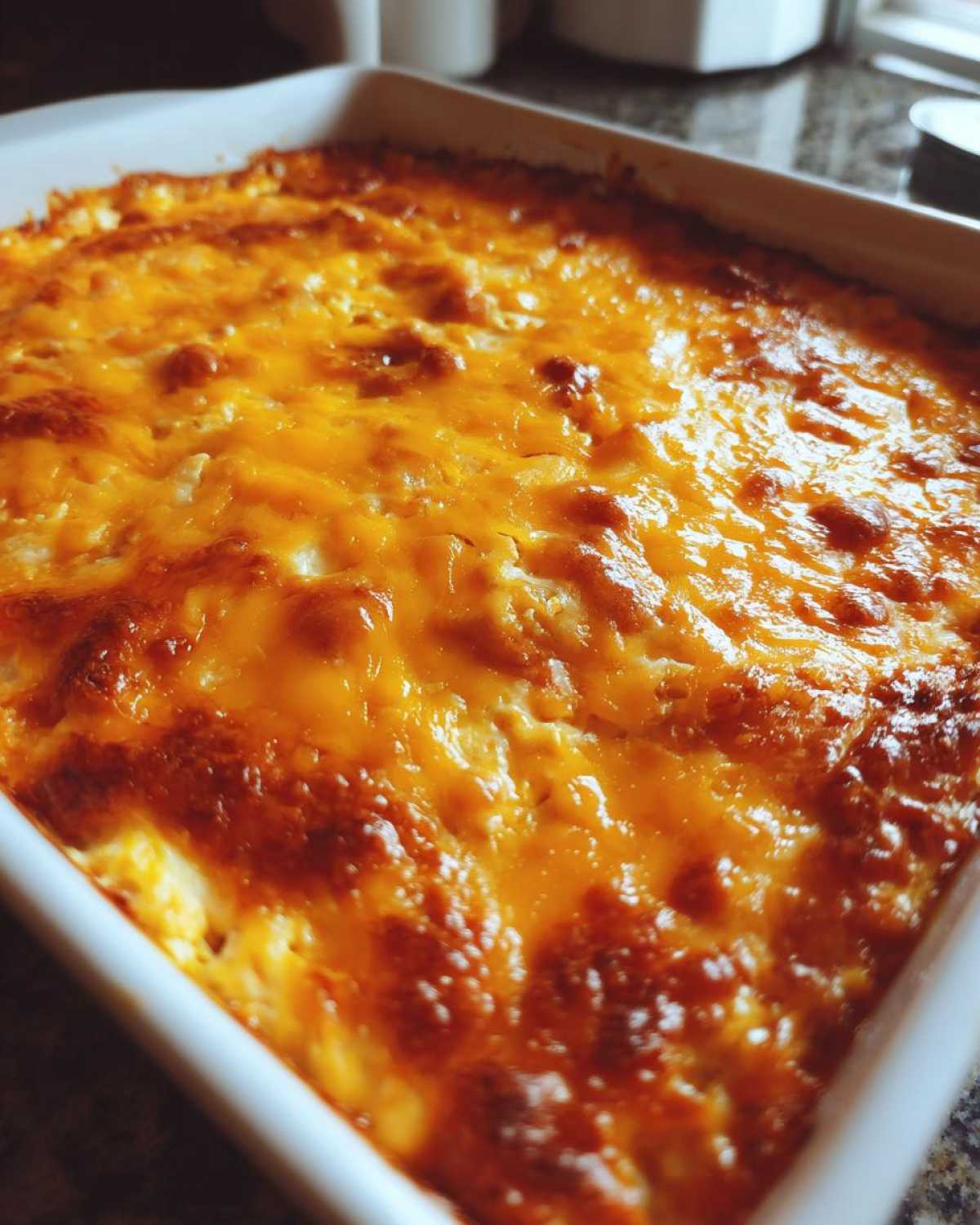 Close-up of a bubbly, baked 3 ingredient chili cheese dip topped with melted, browned cheddar cheese in a white baking dish.