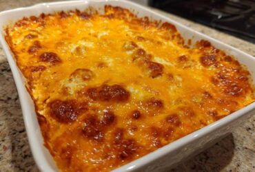 A close-up of a hot, bubbly 3 ingredient chili cheese dip topped with melted, browned cheddar cheese in a white baking dish.