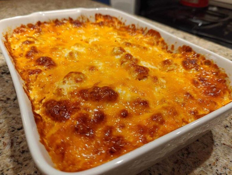 A close-up of a hot, bubbly 3 ingredient chili cheese dip topped with melted, browned cheddar cheese in a white baking dish.