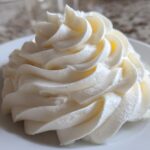 Close-up of a perfectly piped swirl of white, smooth cream cheese frosting on a white plate.