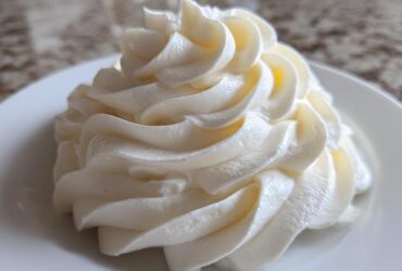 Close-up of a perfectly piped swirl of white, smooth cream cheese frosting on a white plate.
