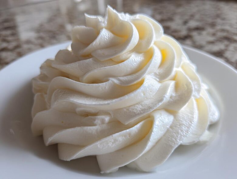 Close-up of a perfectly piped swirl of white, smooth cream cheese frosting on a white plate.