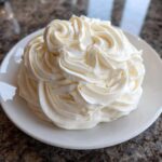 A mound of fluffy, white cream cheese frosting piped into decorative swirls on a small white plate.