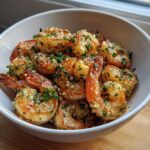 A white bowl filled with perfectly cooked air fryer frozen shrimp seasoned with garlic and fresh parsley.