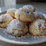 A stack of freshly baked cannoli cookies generously dusted with powdered sugar on a white plate.