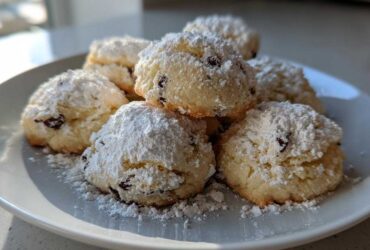 A stack of freshly baked cannoli cookies generously dusted with powdered sugar on a white plate.