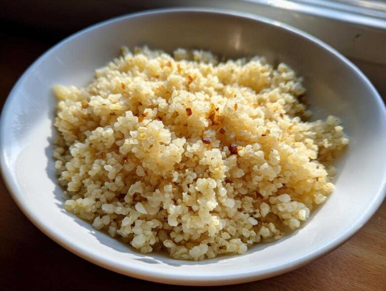 A close-up of fluffy, lightly browned cauliflower rice served in a white bowl, ready to eat.