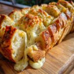 Close-up of a loaf of baked cheese bread, sliced and pulled apart with melted cheese stretching out.