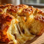 Close-up of a golden-brown, baked cheese bread being pulled apart, showing long, gooey cheese strings.