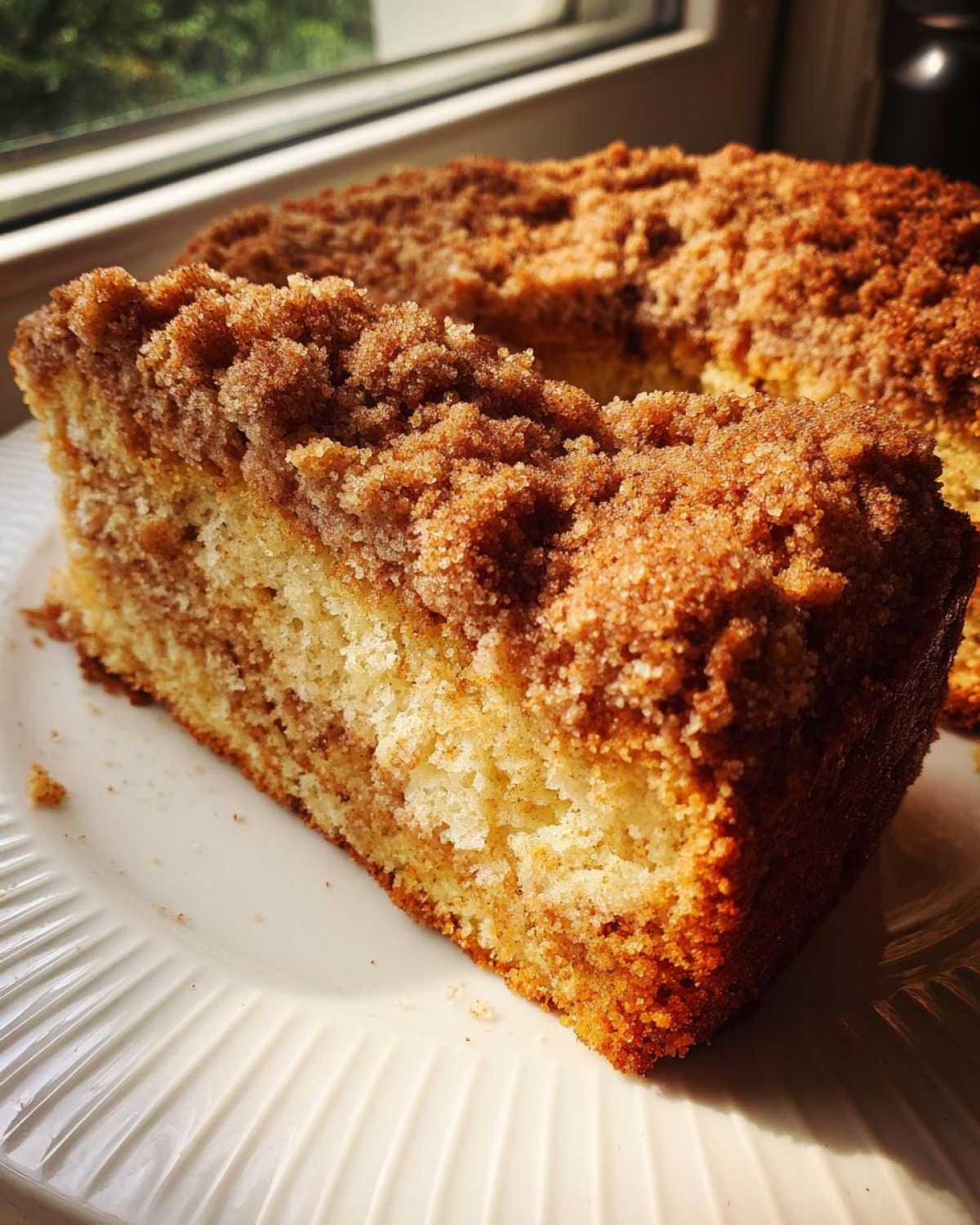 A close-up slice of moist coffee cake featuring a thick, sugary cinnamon crumb topping.