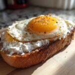 Close-up of a delicious egg toast featuring a fried egg with a runny yolk over a layer of white cheese on toasted bread.