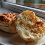 Close-up of a homemade english muffin, split open to show the signature open, airy crumb structure.