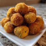 A mound of golden brown, crispy fried okra balls piled high on a small white rectangular plate.