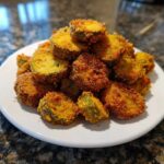 A mound of golden brown, crispy fried okra slices served on a white plate.