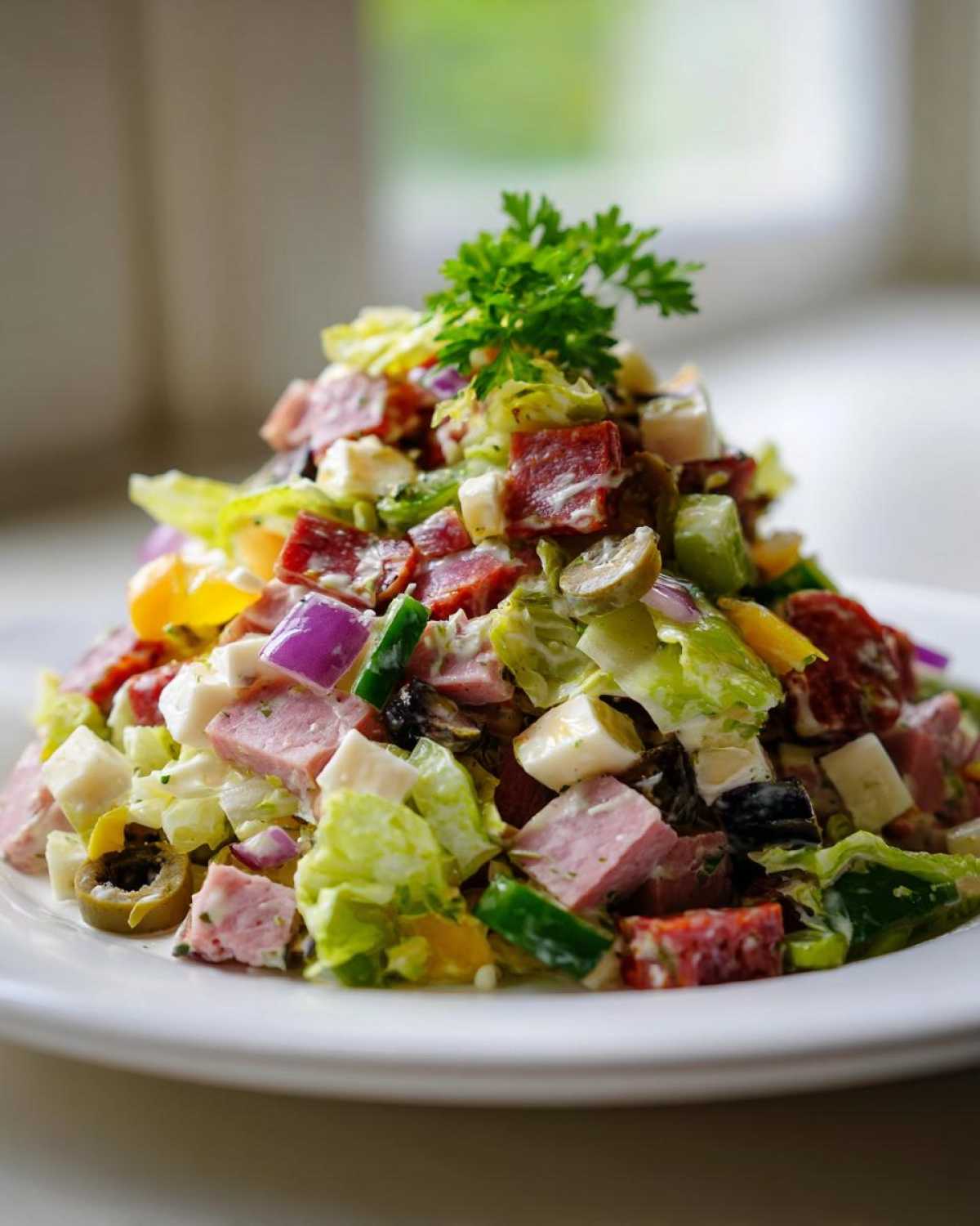 A mound of colorful grinder salad featuring chopped meats, cheese, lettuce, onions, and olives, topped with parsley.