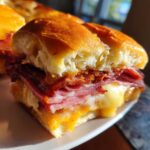Close-up of a baked grinder slider cut in half, showing melted cheese and layers of deli meat inside a soft roll.