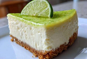 A close-up shot of a perfect slice of key lime cheesecake on a white plate, topped with lime glaze and a fresh lime slice.
