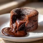 Close-up of a rich chocolate lava cake with molten center pouring out onto a white plate.
