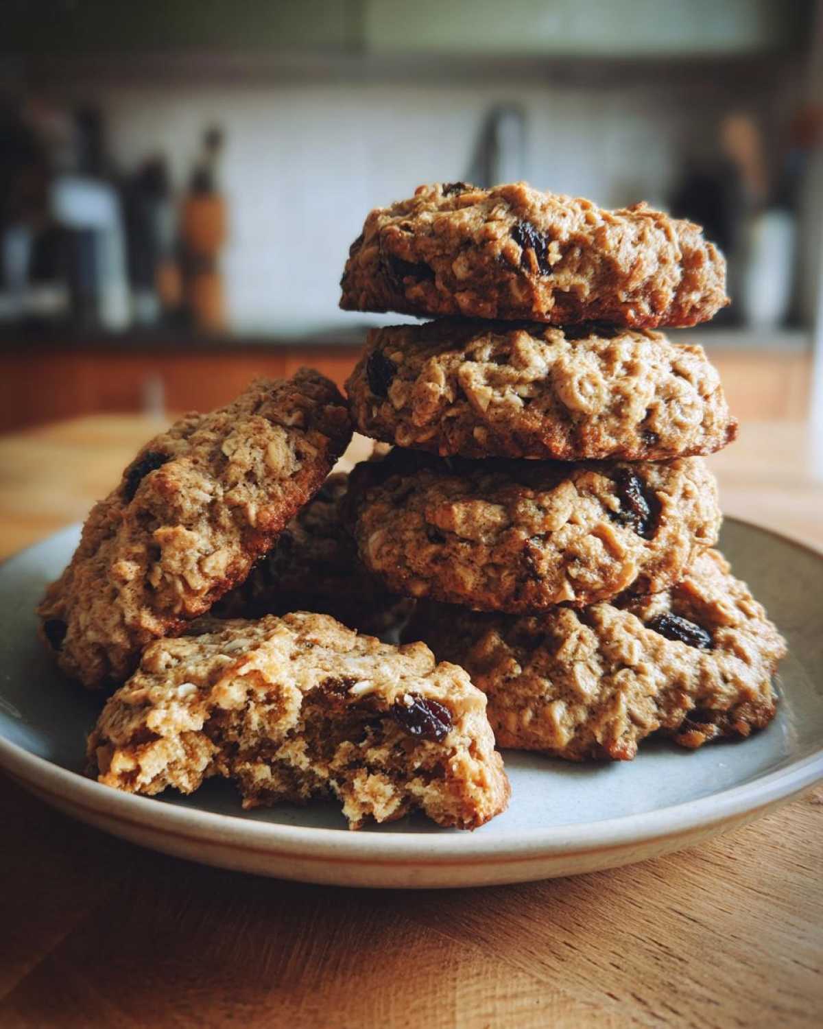 A stack of freshly baked oatmeal raisin cookies piled on a light blue plate, with one cookie having a bite taken out.