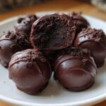 A stack of decadent chocolate-dipped Oreo balls, one cut open to show the dark filling.