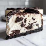 A perfect slice of creamy Oreo cheesecake with visible cookie chunks, sitting on a marble surface.