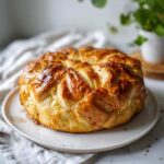 A beautifully golden brown baked brie in puff pastry, glistening on a white plate.