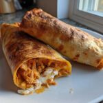 Two golden brown, crispy Baked Chicken Chimichangas served on a white plate, one cut open showing shredded chicken filling.