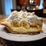 A generous slice of banana cream pie showing custard, banana slices, and a tall topping of whipped cream.