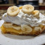 A generous slice of banana cream pie topped with thick whipped cream and fresh banana slices.