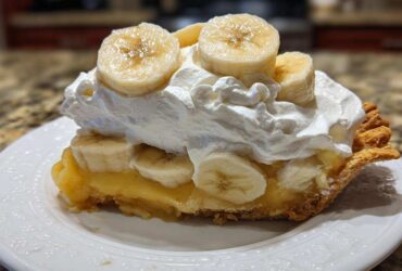 A generous slice of banana cream pie topped with thick whipped cream and fresh banana slices.